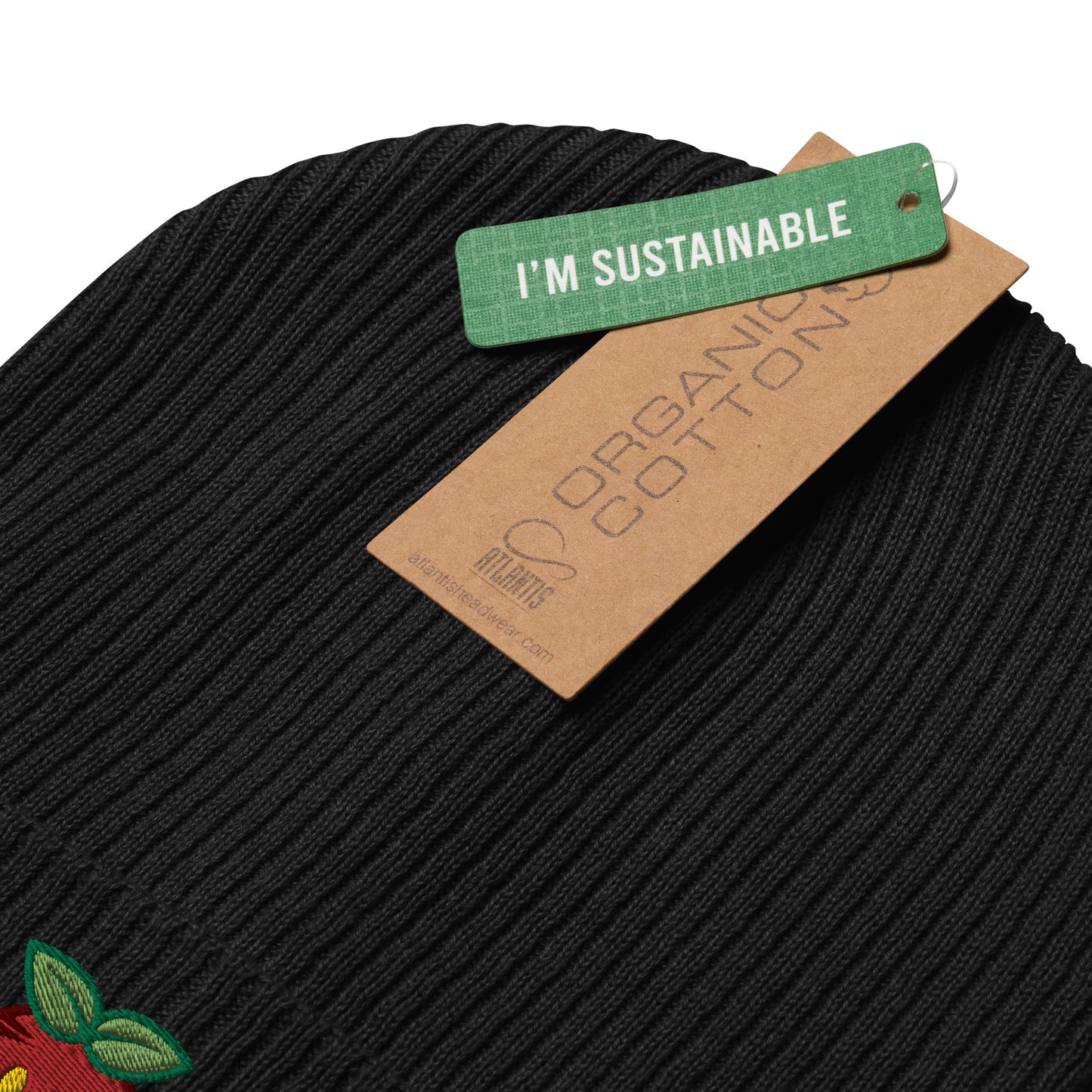 Close-up of a black ribbed beanie adorned with a brown tag labeled "Organic Cotton" and a green tag stating "I'm Sustainable"..